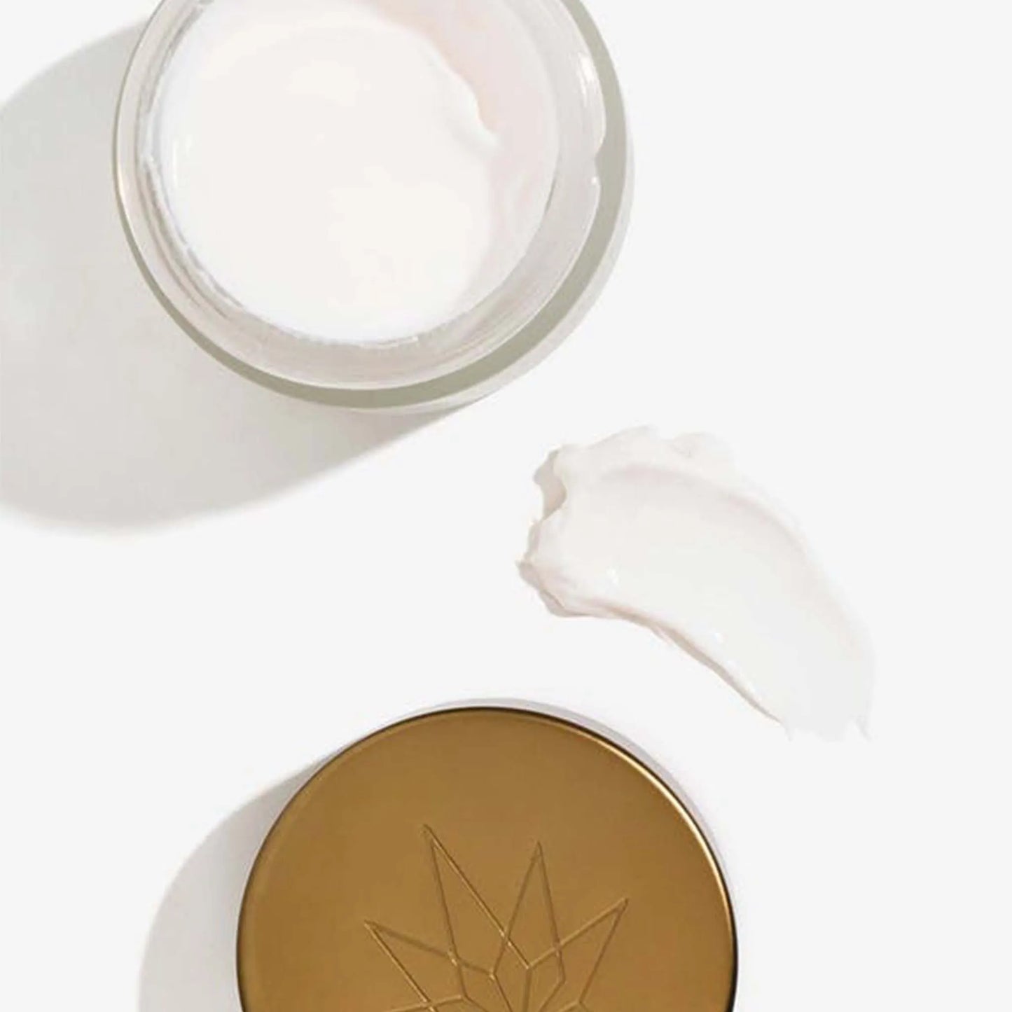 Una caja abierta y la tapa de la Crema de Noche - CBD & Vitamina E yacen junto a una mancha de la crema.