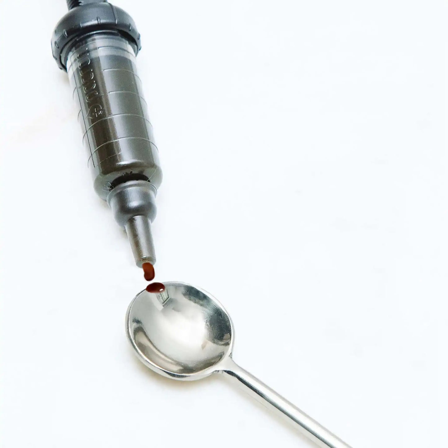 Jeringa dosificadora derramando gotas de aceite en una cuchara de metal