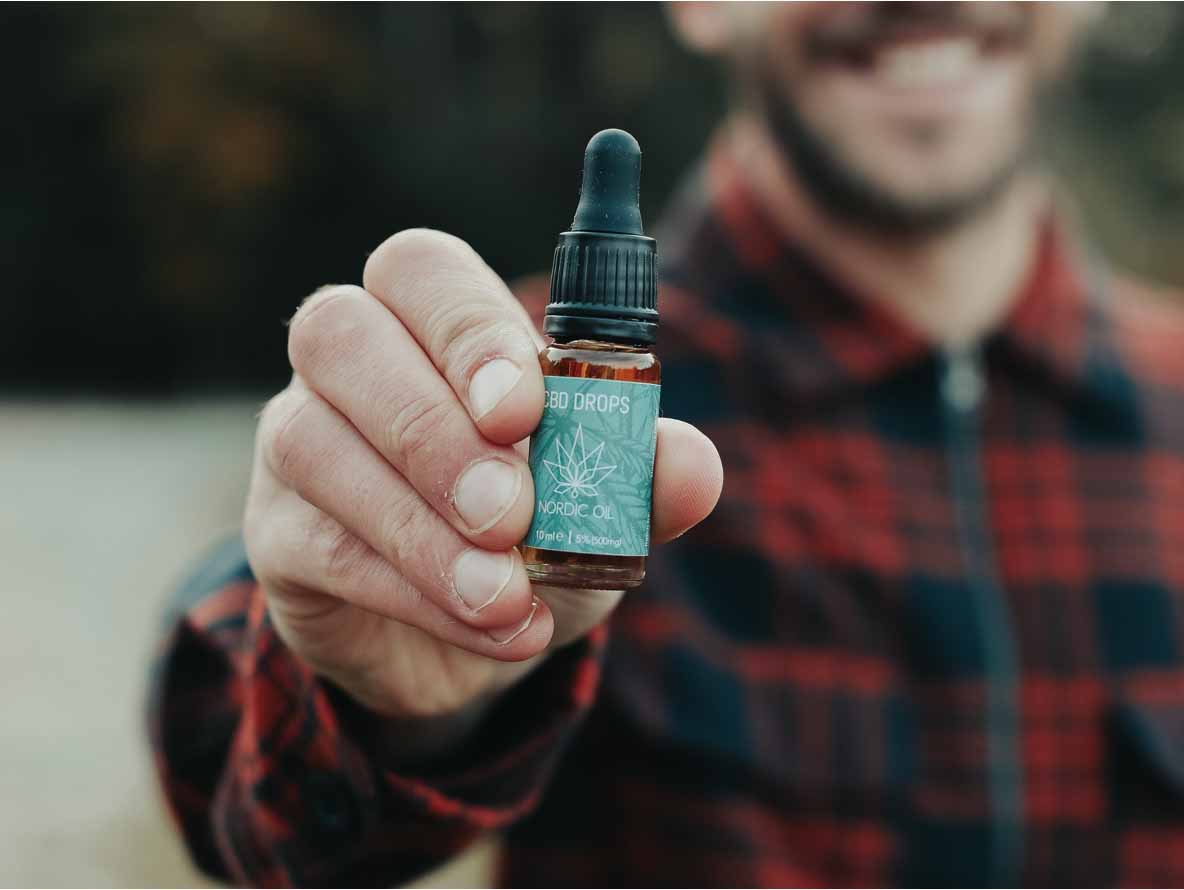 Un hombre sostiene un frasco de aceite de CBD de Nordic Oil.