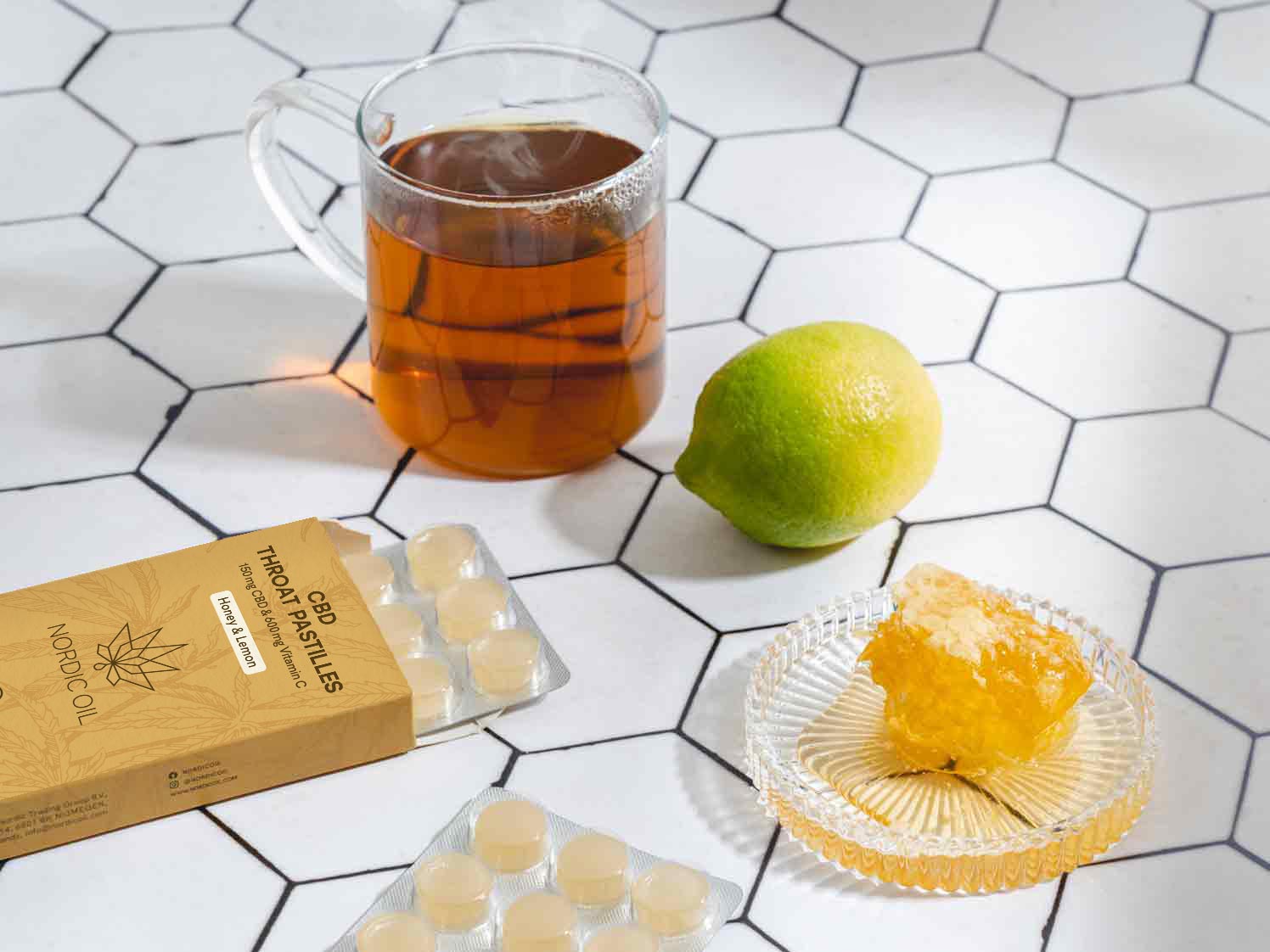 Un vaso de té junto a una lima, miel y las pastillas para la garganta CBD.
