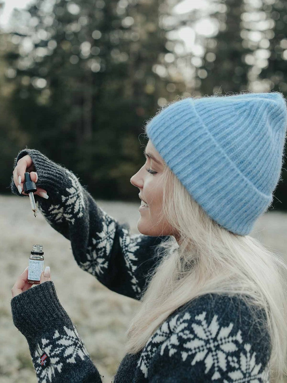 Mujer con gorro azul y suéter de invierno sosteniendo un frasco de aceite de CBD con gotero al aire libre