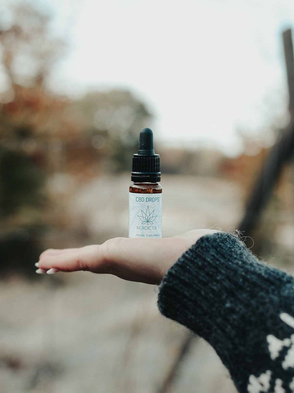 Frasco de CBD con cuentagotas sobre la palma de una mano al aire libre.