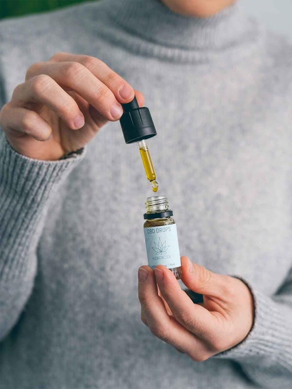 Persona con suéter gris usando un cuentagotas para dispensar aceite de CBD de un frasco.
