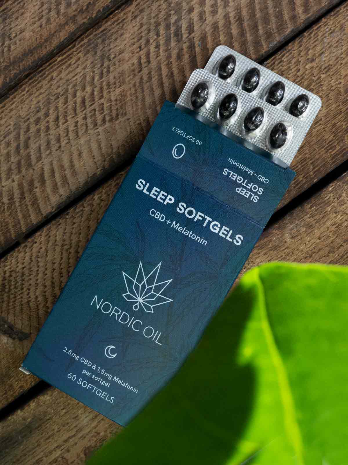 Caja azul de Nordic Oil Sleep Softgels con CBD y melatonina, junto a un blíster de cápsulas sobre una superficie de madera