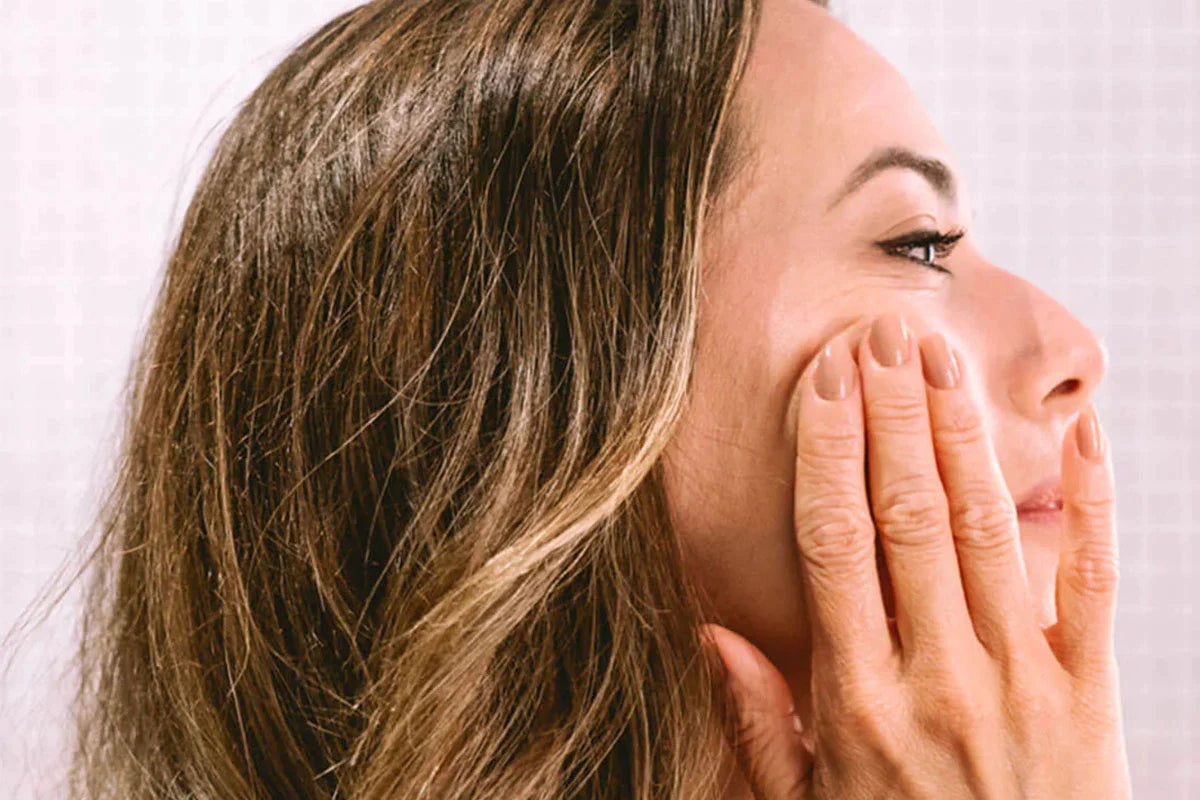 Una mujer se aplica Crema Facial Antiarrugas - CBD y Retinol en las mejillas. 