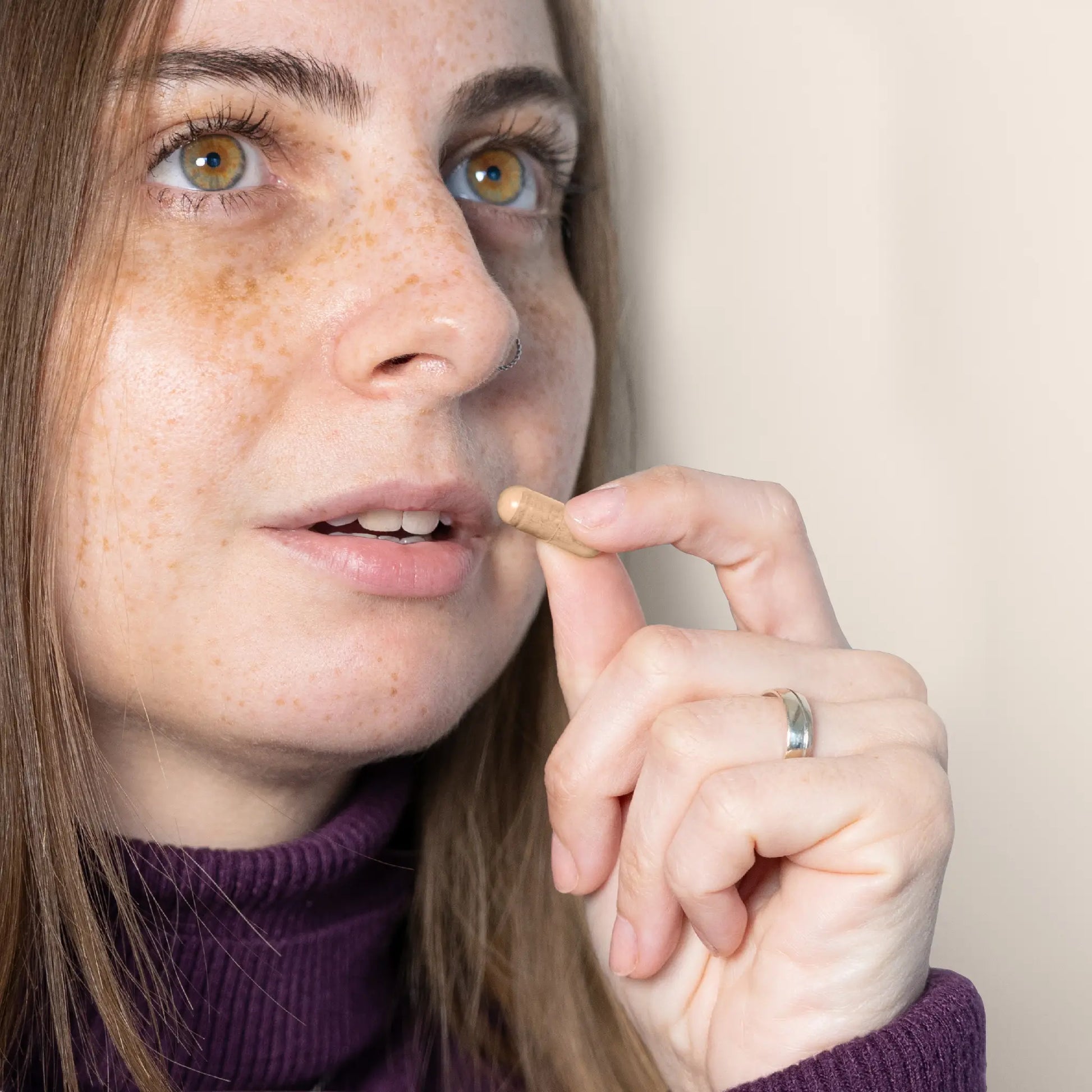 Mujer con pecas sosteniendo una cápsula beige junto a la boca