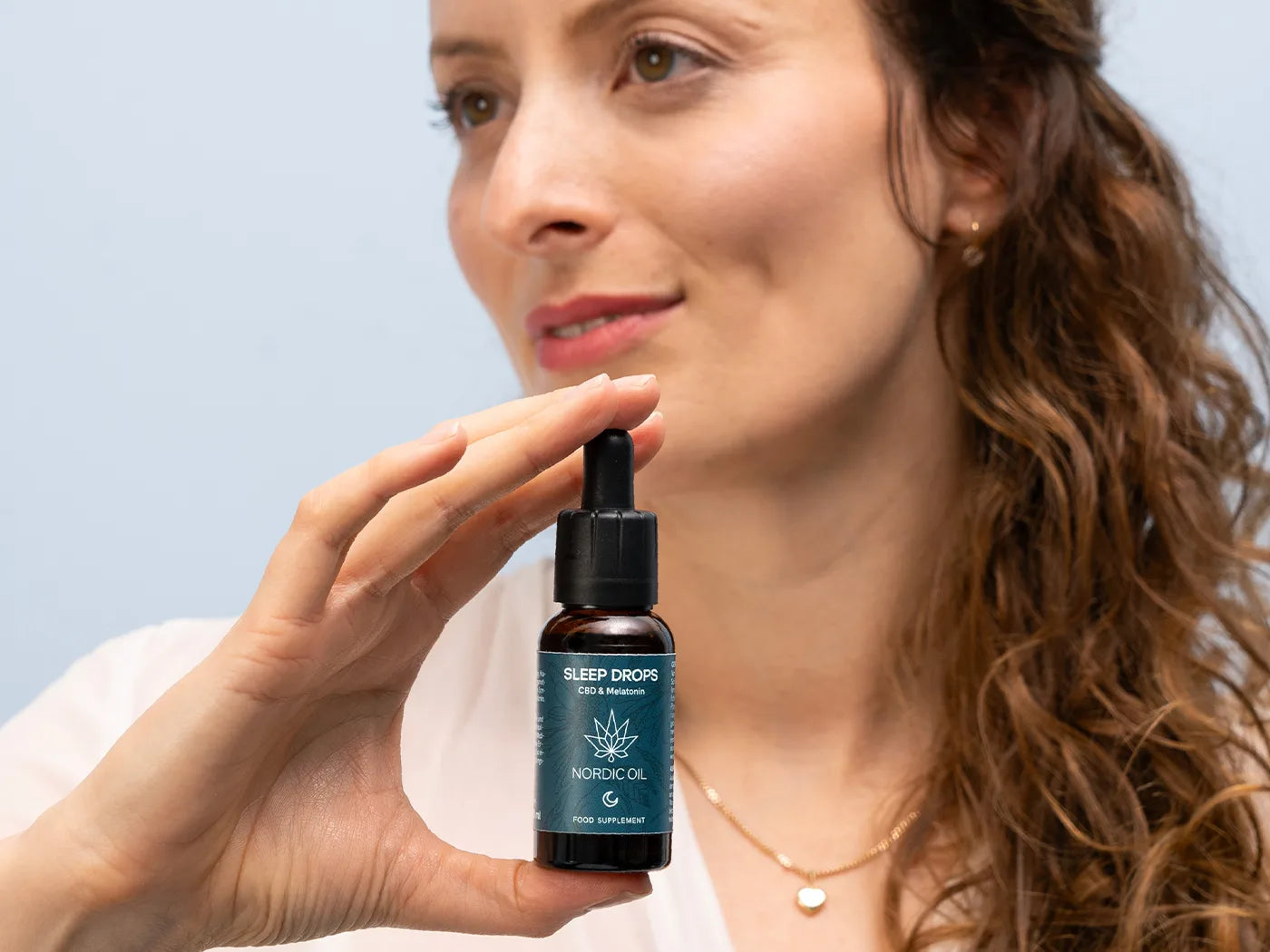Mujer sosteniendo un frasco oscuro con gotero de Nordic Oil Sleep Drops (CBD y melatonina)
