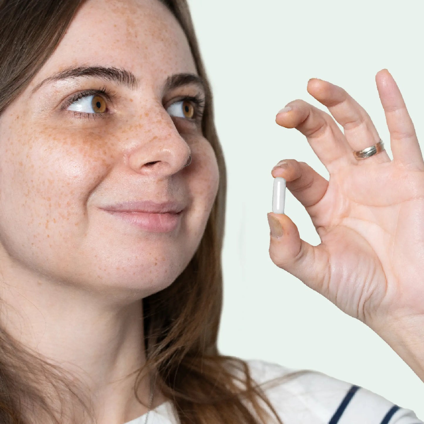 Mujer joven con pecas sosteniendo una cápsula blanca entre los dedos